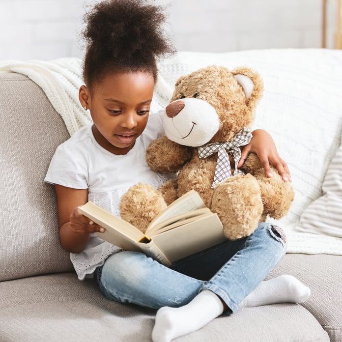 Adorable black kid with teddy bear reading book